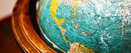 A globe displays North and Central America, highlighting countries in various colors. It rests in a wooden stand, suggesting an educational or decorative setting indoors.