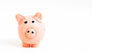A small pink piggy bank stands on a white surface, facing forward, with a soft shadow underneath. The background is minimal and brightly lit.