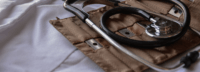 A stethoscope rests on a folded brown fabric case, placed on a white cloth surface, suggesting a medical setting or preparation for examination.