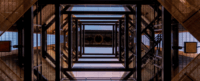 Metallic stairwell spirals upward, viewed from below, creating geometric patterns. The structure's grid-like framework is contrasted against a clear blue sky, emphasizing architectural symmetry.