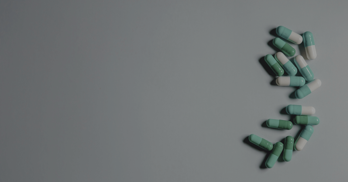 Capsules are scattered on a smooth, grey surface. The pills alternate between green and white halves, lying in a loose cluster on the right side.