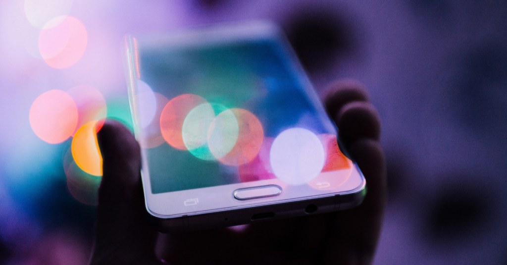 A hand holding a smartphone with colorful bokeh lights in the background.