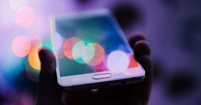 A hand holding a smartphone with colorful bokeh lights in the background.