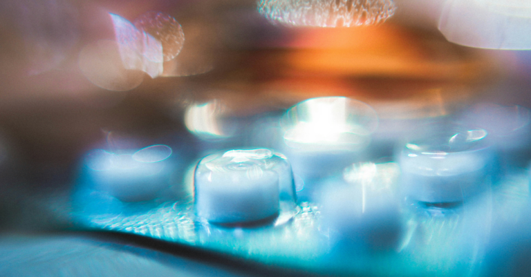 Ice cubes floating in blue water with warm, blurred lights in the background.