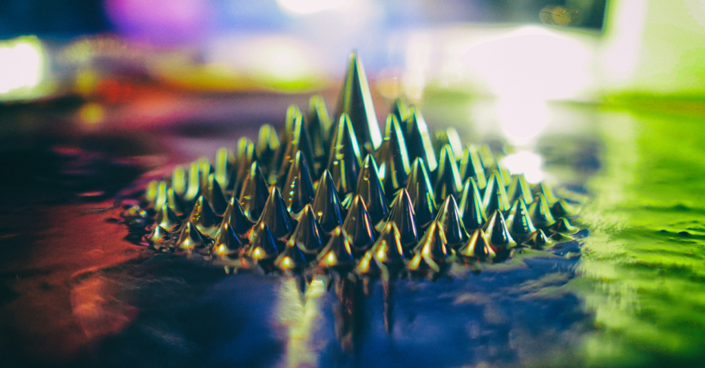 Close-up of a spiked metal cone sculpture resting on a glossy, rainbow-lit surface.