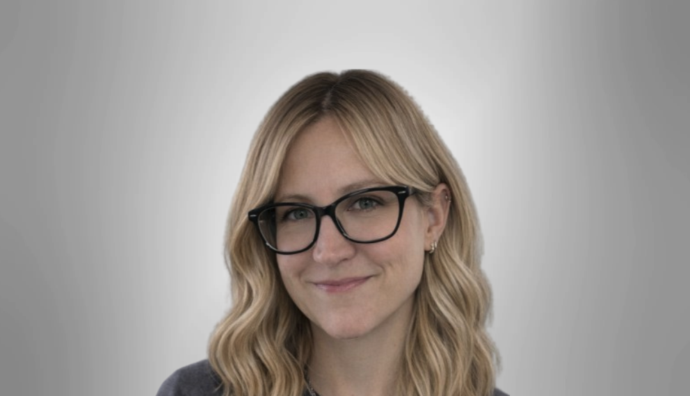 Smiling woman with shoulder-length blonde hair and glasses against a light gray background.