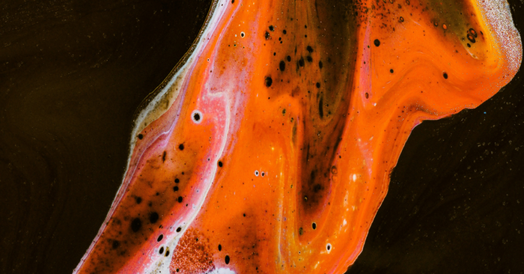Close-up of orange and white liquid with black speckles flowing on a dark background.