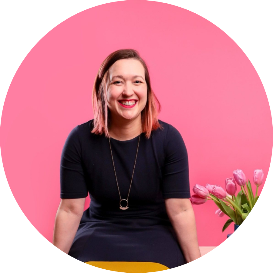 Smiling woman in a navy dress sits against a pink background with pink tulips on her right.