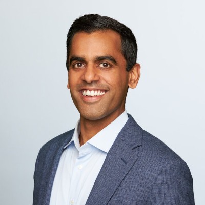 Portrait of a smiling man in a blue blazer and white shirt against a light gray background.